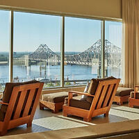 A warm and inviting hotel lounge with large windows offering a panoramic view of a truss bridge over a tranquil river.